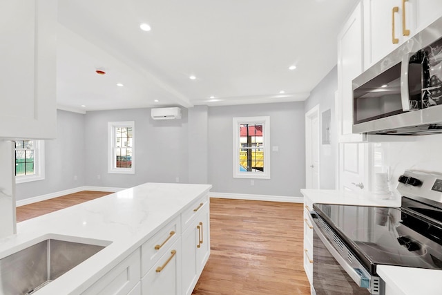 3780 Willett Ave, Bronx, NY 10467 - kitchen featuring stainless steel appliances, an AC wall unit, light wood-style floors, baseboards, and white cabinetry