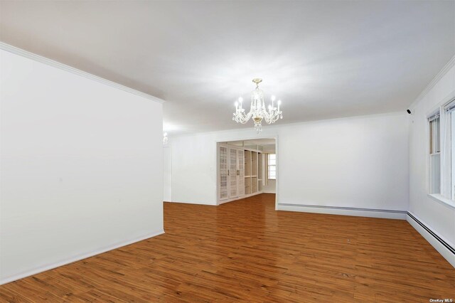 empty room featuring a chandelier, wood finished floors, ornamental molding, and a baseboard radiator