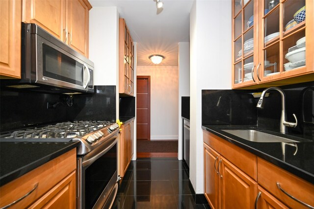 kitchen with stainless steel appliances, a sink, decorative backsplash, glass insert cabinets, and dark tile patterned flooring