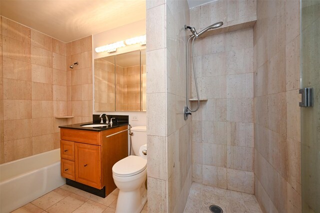full bath with a tile shower, vanity, toilet, tile patterned floors, and tile walls