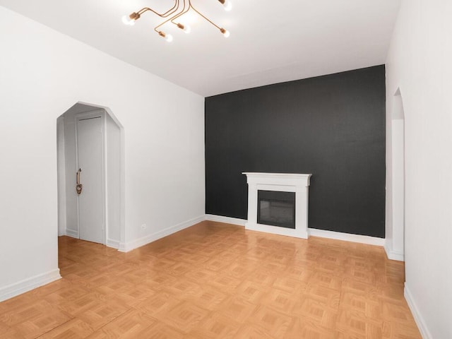 unfurnished living room with baseboards, a glass covered fireplace, and arched walkways