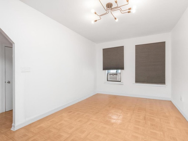 empty room featuring a chandelier, baseboards, and cooling unit