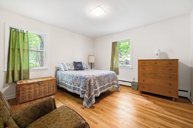 bedroom featuring baseboard heating, wood finished floors, and multiple windows