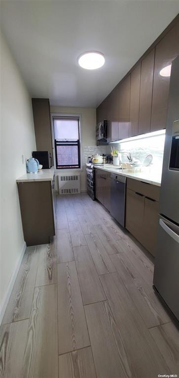 kitchen featuring radiator heating unit, light wood-style floors, light countertops, and stainless steel appliances