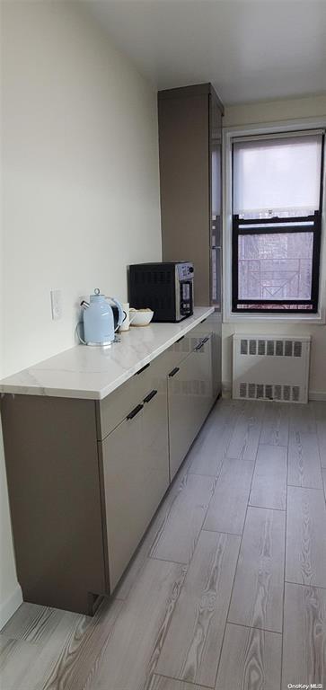 kitchen featuring radiator, wood tiled floors, light countertops, and stainless steel microwave