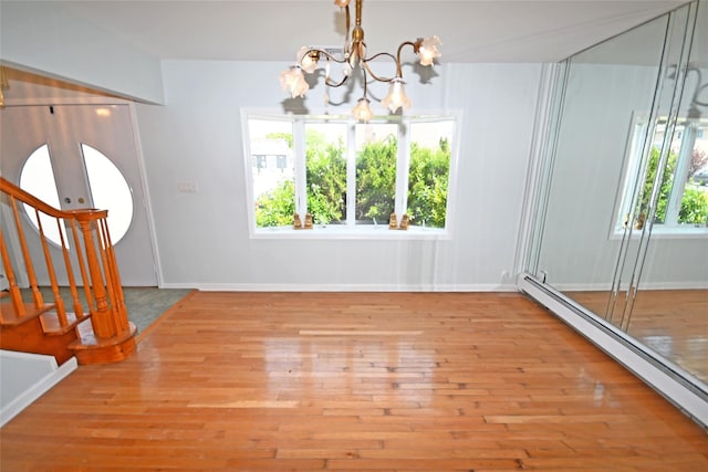 unfurnished dining area with a baseboard heating unit, a chandelier, wood finished floors, and stairway