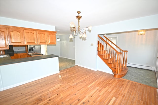 kitchen featuring stainless steel refrigerator with ice dispenser, a baseboard heating unit, dark countertops, a chandelier, and light wood-type flooring