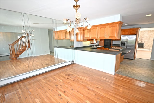 kitchen featuring stainless steel refrigerator with ice dispenser, a chandelier, dark countertops, light wood finished floors, and a sink