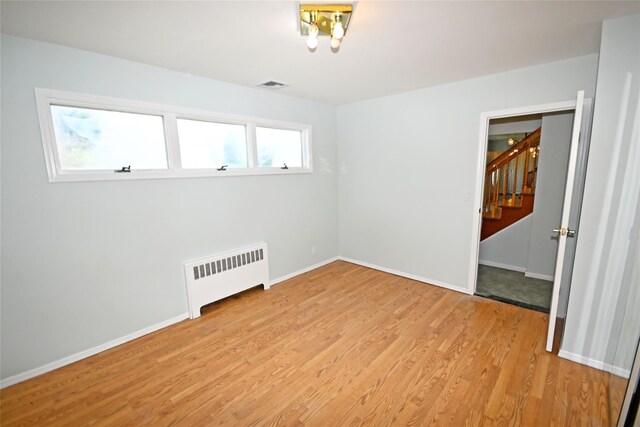 empty room with radiator, light wood-style floors, stairs, and baseboards