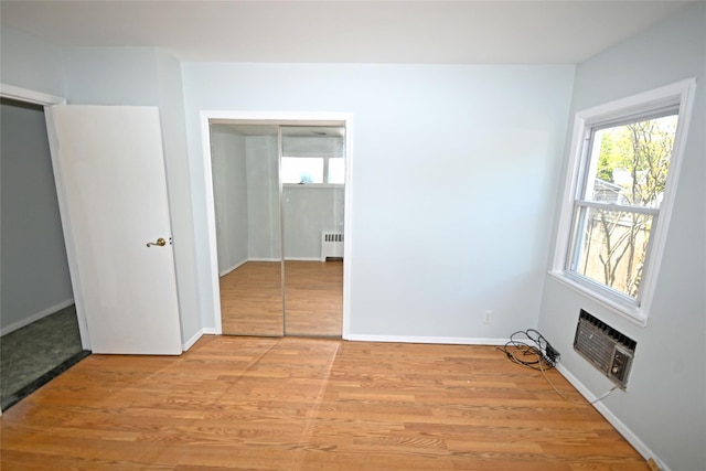 unfurnished bedroom featuring radiator heating unit, light wood-style flooring, an AC wall unit, and baseboards