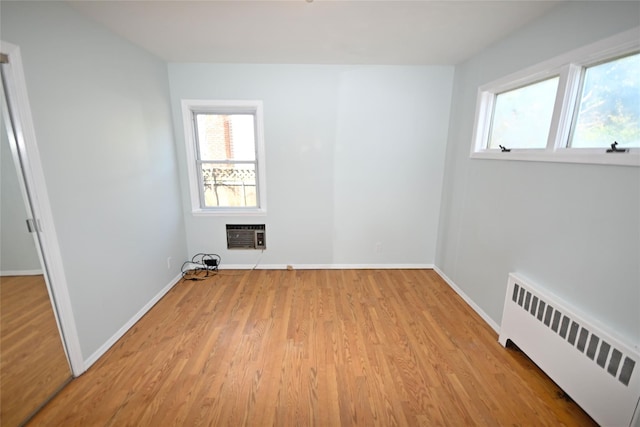empty room with radiator heating unit, wood finished floors, baseboards, and a wall mounted air conditioner