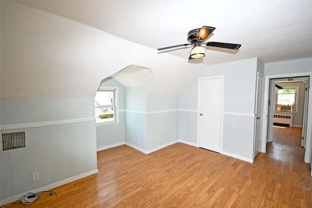 additional living space with radiator, light wood-type flooring, baseboards, ceiling fan, and lofted ceiling