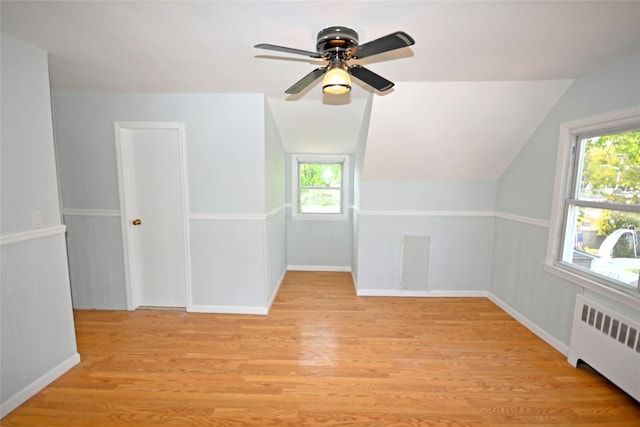 additional living space with radiator heating unit, light wood-type flooring, healthy amount of natural light, and vaulted ceiling