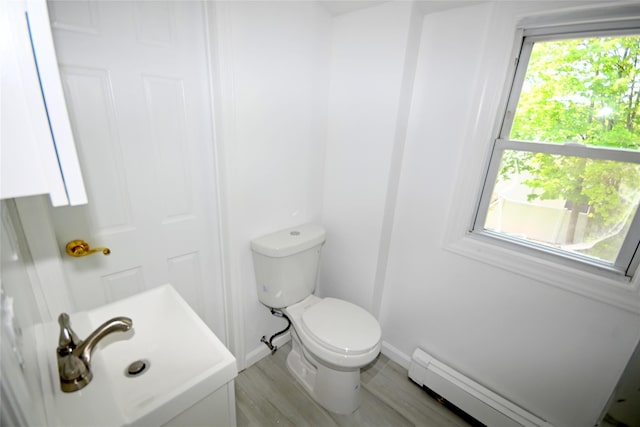 half bath featuring baseboard heating, toilet, wood finished floors, and baseboards