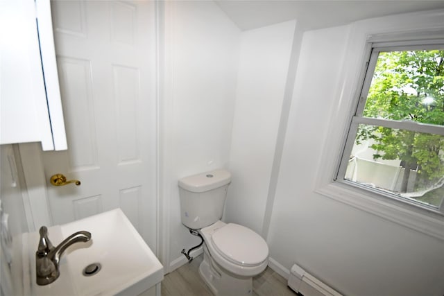bathroom featuring toilet, baseboards, wood finished floors, a baseboard heating unit, and a sink