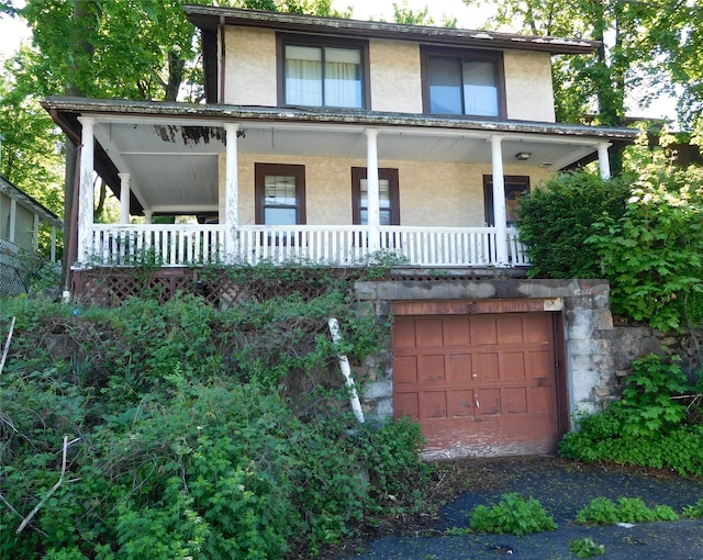 view of front facade with stucco siding, a porch, and an attached garage