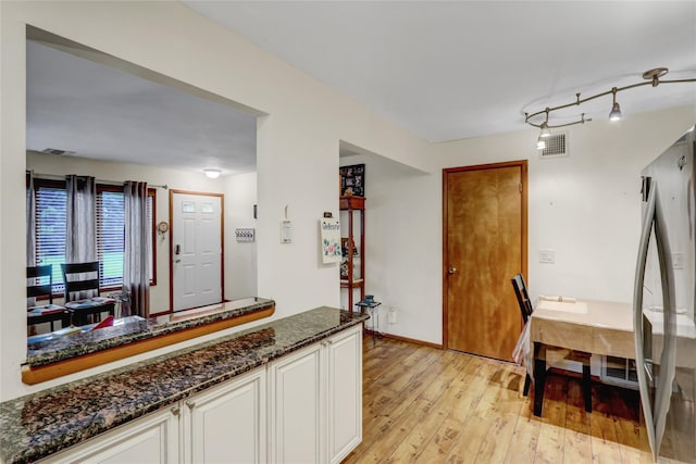 kitchen with freestanding refrigerator, dark stone counters, light wood-type flooring, and white cabinetry