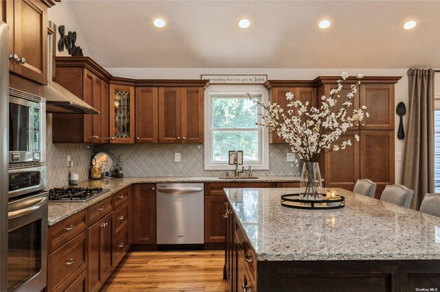 kitchen featuring stainless steel appliances, a sink, a kitchen island, light wood finished floors, and recessed lighting