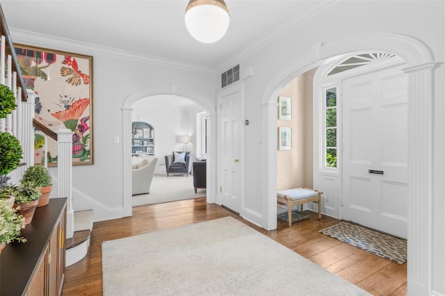 foyer entrance with arched walkways, wood-type flooring, crown molding, baseboards, and ornate columns