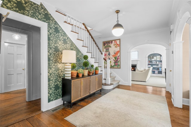 foyer with a warm lit fireplace, arched walkways, baseboards, wood finished floors, and ornamental molding