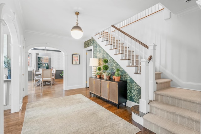 foyer with arched walkways, wood finished floors, ornamental molding, stairs, and baseboards