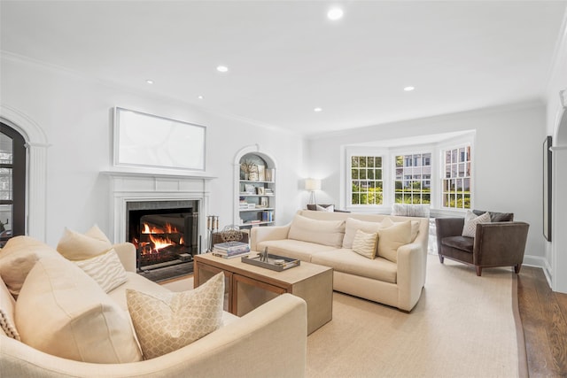 living area featuring crown molding, a warm lit fireplace, light wood-style flooring, and recessed lighting