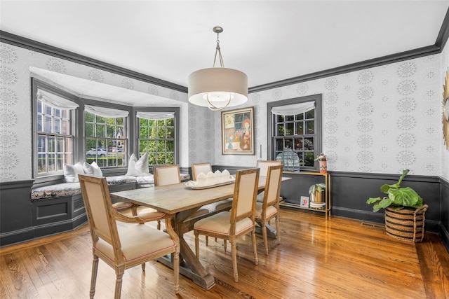 dining space featuring wallpapered walls, a wainscoted wall, wood finished floors, and crown molding