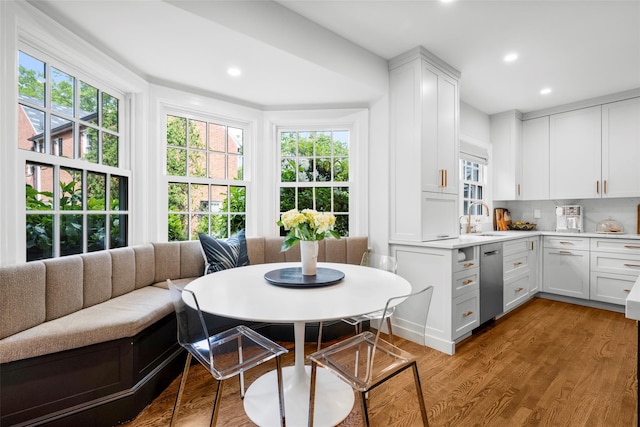kitchen featuring stainless steel dishwasher, a sink, white cabinets, plenty of natural light, and recessed lighting