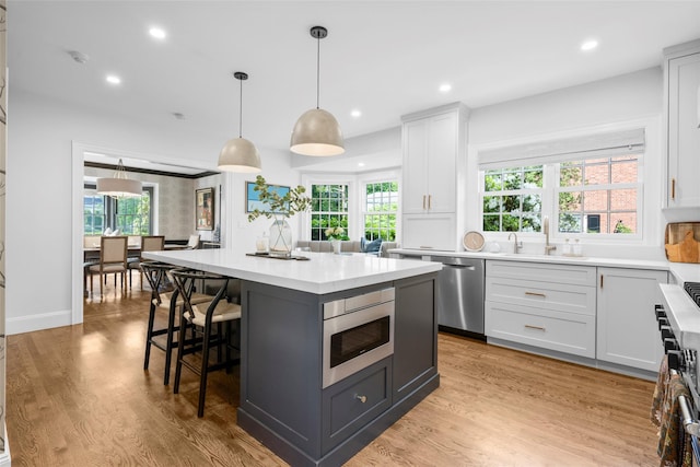 kitchen with a sink, stainless steel appliances, light countertops, a kitchen island, and white cabinets