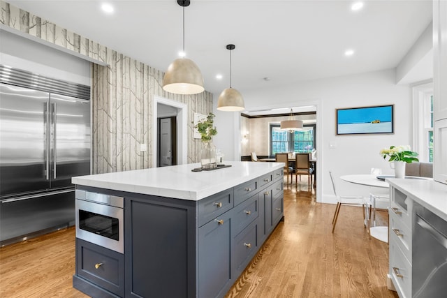 kitchen featuring appliances with stainless steel finishes, light countertops, light wood-style flooring, a center island, and recessed lighting
