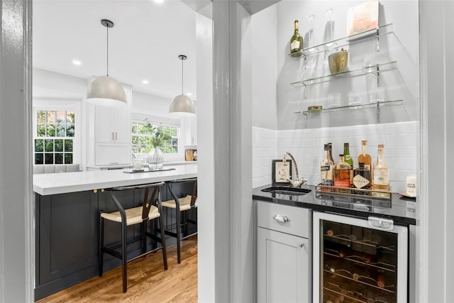 indoor bar with beverage cooler, tasteful backsplash, light wood finished floors, decorative light fixtures, and recessed lighting