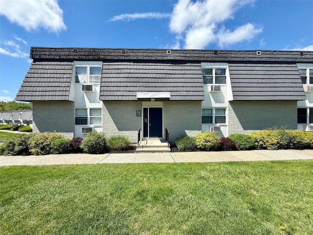 view of front of property with brick siding, mansard roof, and a front lawn