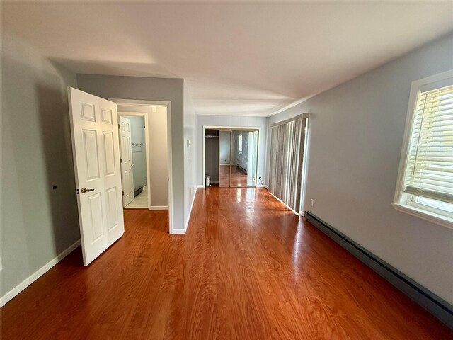 corridor with a baseboard radiator, wood finished floors, and baseboards