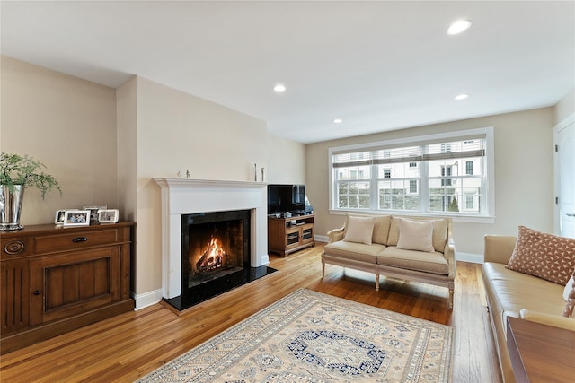 living area with a lit fireplace, light wood-type flooring, recessed lighting, and baseboards