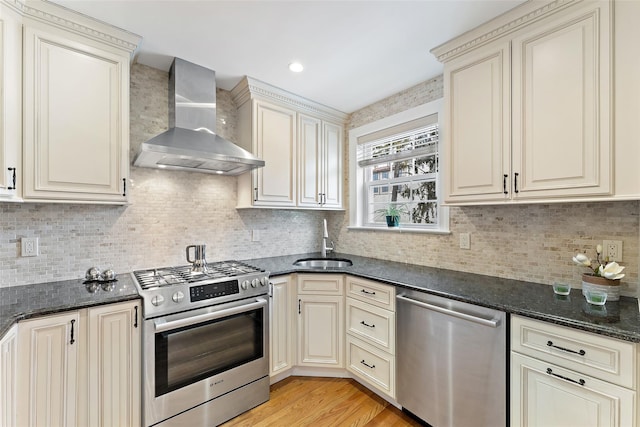 kitchen featuring stainless steel appliances, wall chimney range hood, a sink, and cream cabinetry