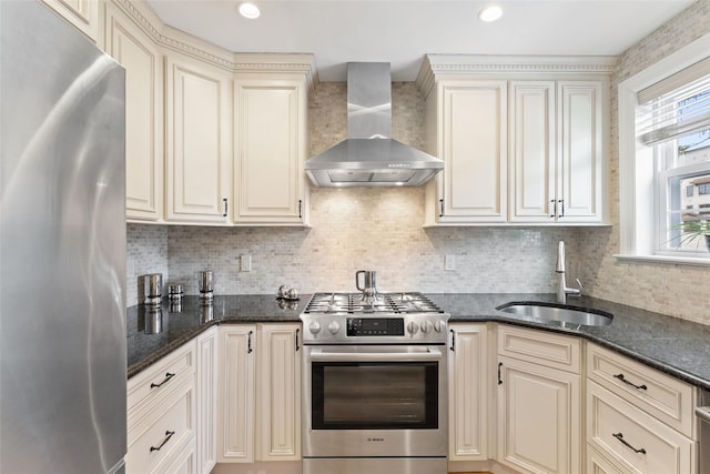 kitchen featuring stainless steel appliances, a sink, wall chimney exhaust hood, cream cabinets, and tasteful backsplash