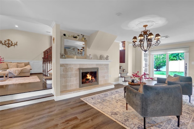 living area with stairs, wood finished floors, a tile fireplace, and a chandelier