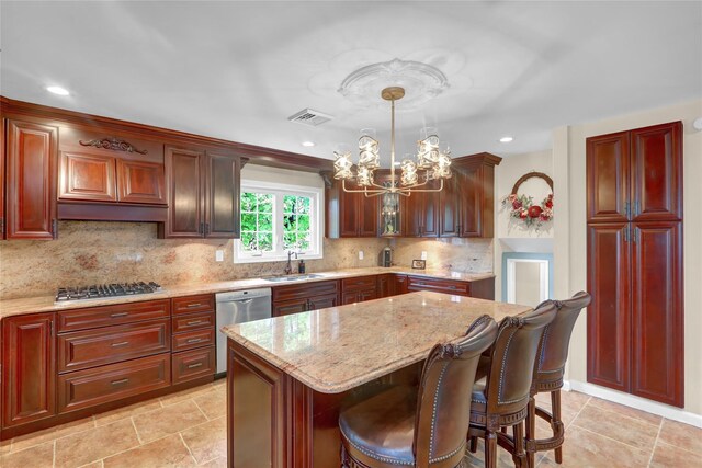 kitchen with appliances with stainless steel finishes, a sink, a chandelier, light stone countertops, and a kitchen bar