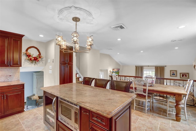 kitchen featuring stainless steel microwave, dark brown cabinets, a kitchen island, vaulted ceiling, and a chandelier
