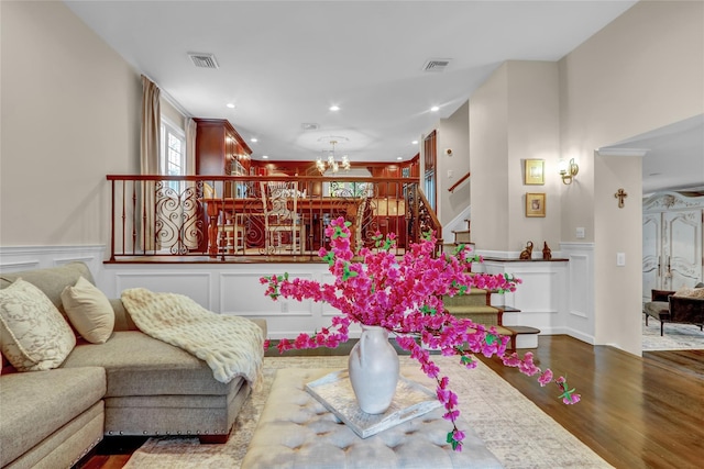 living room featuring a decorative wall, a chandelier, wood finished floors, stairs, and a wainscoted wall