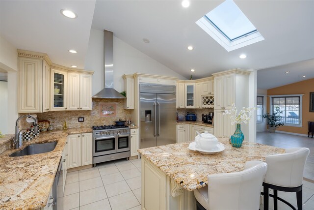kitchen with cream cabinets, premium appliances, vaulted ceiling, wall chimney range hood, and a sink