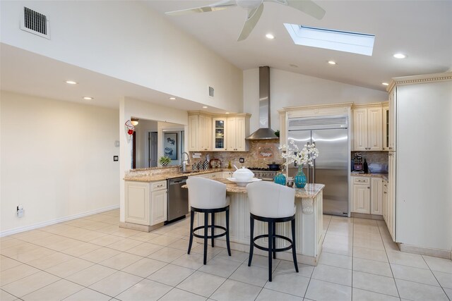 kitchen with appliances with stainless steel finishes, wall chimney exhaust hood, cream cabinetry, backsplash, and lofted ceiling