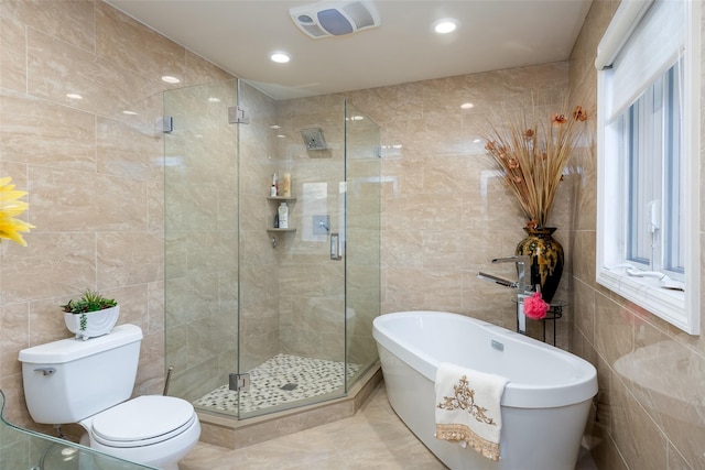 full bathroom with tile walls, a shower stall, a freestanding tub, and toilet
