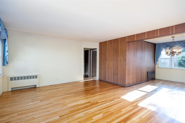 unfurnished room with radiator heating unit, a chandelier, light wood-style floors, and wooden walls