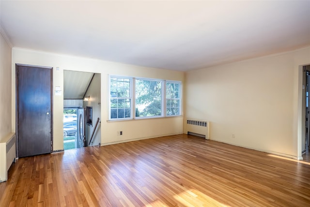 unfurnished living room with radiator heating unit, wood finished floors, ornamental molding, and baseboards