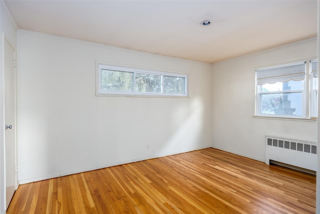 empty room with radiator, plenty of natural light, light wood-type flooring, and ornamental molding