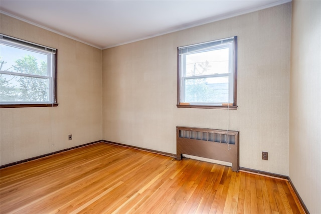empty room featuring radiator heating unit, light wood-style floors, and crown molding