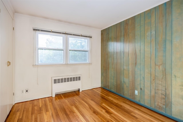 unfurnished room featuring radiator heating unit, wood finished floors, crown molding, and baseboards