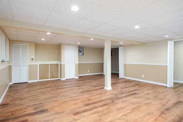 finished basement with light wood-type flooring, baseboards, recessed lighting, and a drop ceiling