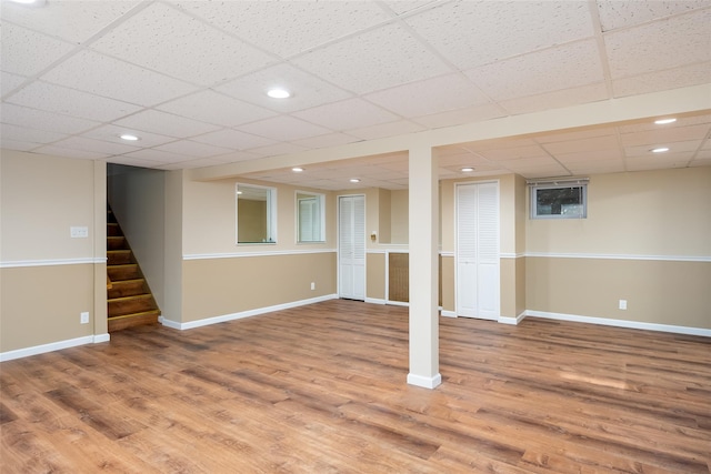 finished below grade area with light wood-style flooring, stairs, baseboards, a paneled ceiling, and recessed lighting